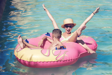 Mother and son enjoying their holidays in waterpark. They are swimming in a rubber ring along the...