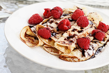 Delicious golden palacinky pancakes or Czech Pancakes with fresh raspberries and sweet chocolate syrup. Extreme shallow depth of field.