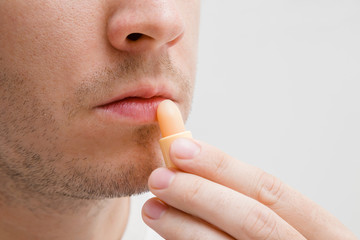 Handsome, young, bearded man using natural lips balm on light gray background. Care about healthy,...