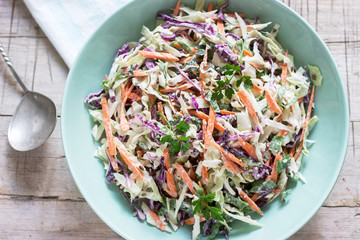 Coleslaw of cabbage, carrots and various herbs with mayonnaise in a large plate on a wooden background. - obrazy, fototapety, plakaty