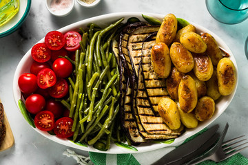 a side dish of vegetables on the holiday table. healthy food for the whole family or dinner at a restaurant on a white marble table. baked potatoes, grilled eggplants, cherry tomato salad 