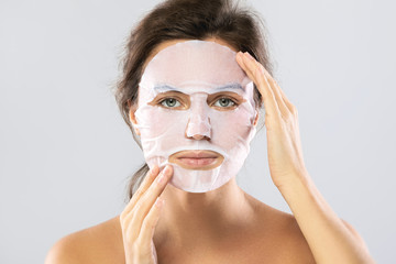 Woman with a sheet moisturizing mask on her face isolated on gray background