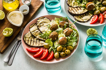 an appetizing dinner or lunch from a salad with tomatoes, grilled eggplants and legume falafel with sesame tahini dressing. Vegan healthy food for the whole family