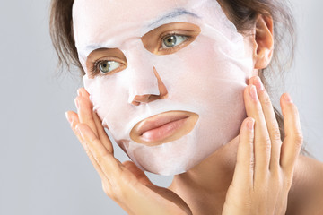 Woman with a sheet moisturizing mask on her face isolated on gray background