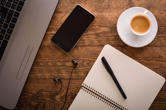 Cup of coffee on a laptop keyboard. Work place modern. Laptop (notebook) with cup of coffee and notepad with pen on old wooden table.