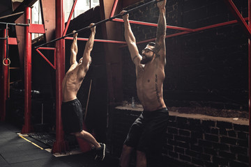 Two strong men doing exercise on bars in the gym