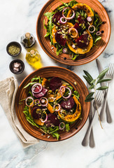 warm salad of baked pumpkin and beets with arugula and seeds on a marble table. healthy vegan...