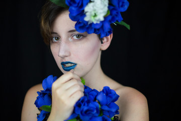 Sensual young woman touching face and looking at camera with blue flowers composition  