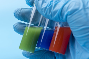 A gloved hand holds three vials of different liquid inside on a blue background.