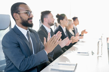 Group of positive excited business people sitting in line and applauding while greeting coach at...