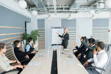 Content attractive sales manager in formal suit standing at whiteboard and pointing at graph while explaining information to colleagues