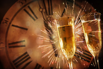 Two champagne glasses against holiday lights and clock at midnight