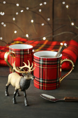 Small toy deer with mugs on rustic holiday background