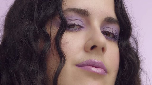 closeup woman with lilac makeup watches aside and then to the camera