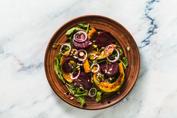 warm salad of baked pumpkin and beets with arugula and seeds on a marble table. healthy vegan cuisine for the whole family