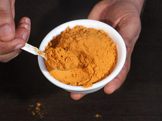 Turmeric in White Bowl in Hand, Turmeric on Wooden background,Turmeric in Spoon on Wooden Background,Turmeric is Good Remedy for Health,