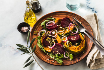 warm salad of baked pumpkin and beets with arugula and seeds on a marble table. healthy vegan cuisine for the whole family