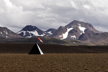 A landing pad for small airplanes is marked in front of a mountain chain with snow remains, a red...