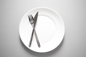 metal knife and fork on clean white plate for restaurant or food meal serving with grey background