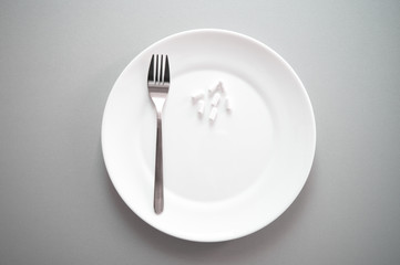 white tablet pill medical drug on plate with fork for food and health gray background