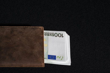 Money in European euro currency is in a brown purse on a black velvet table, a symbol of finance and business.