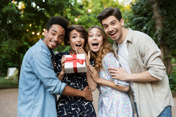 Happy young group of friends outdoors in park having fun holding gift box.
