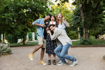 Fototapeta premium Happy young group of friends outdoors in park having fun holding gift box.