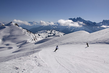Fototapeta na wymiar Skiers in French Alps carve turns as they make their way down a piste in Avoriaz, Portes du Soleil ski area. Swiss Alps can be seen in background