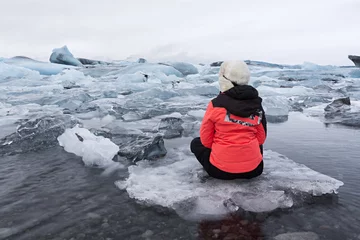 Crédence de cuisine en verre imprimé Glaciers Jeune femme assise dans la lagune glaciaire en Islande.
