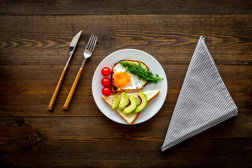 Healthy hearty breakfast. Fried eggs with vegetables near toast with avocado on dark wooden background copy space