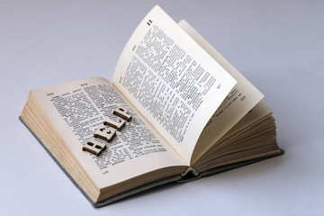 The word HELP from wooden letters is laid out on the page of the book. English-Russian dictionary. The concept of self-learning a foreign language, preparing students for exams. White background.