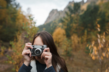 Portrait of a girl with a retro camera on the background of autumn mountains