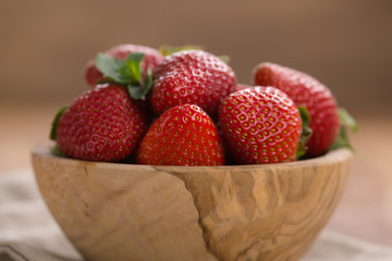 Ripe strawberries in wooden bowl on wood background
