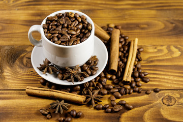 Coffee beans in white cup, cinnamon sticks and star anise on wooden table