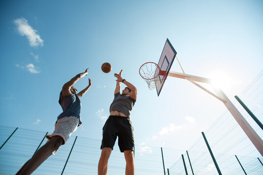 Low angle  of two young men playing basketball and jumping by hoop against blue sky, copy space