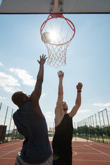 Fototapeta premium Action portrait of two young men playing basketball and jumping by hoop against blue sky lit by sunlight