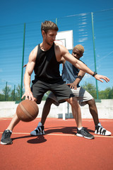 Fototapeta premium Full length action shot of two muscular men playing basketball in outdoor court