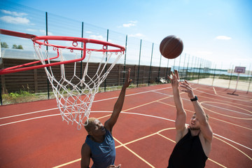 Naklejka premium Portrait of young basketball player throwing ball in basket on outdoor court lit by sunlight, copy space