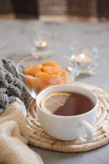 Obraz na płótnie Canvas Cup of tea and dried apricots on a table, candles and knited blanket.