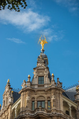 Fototapeta na wymiar Antwerp, Belgium - September 24, 2018: Golden lightning carrying angel statue on top of brown stone facade on corner of Meir and Otto Veniusstraat against blue sky, More statues.