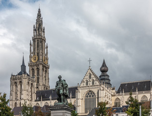 Obraz premium Antwerp, Belgium - September 24, 2018: Peter Paul Rubens bronze statue with towers, nave and chancel of Onze-Lieve-Vrouwe Cathedral of Our Lady in back under white cloudy sky.