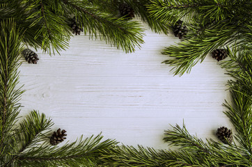 Christmas frame of pine green branches and pine cones on a white wooden background.