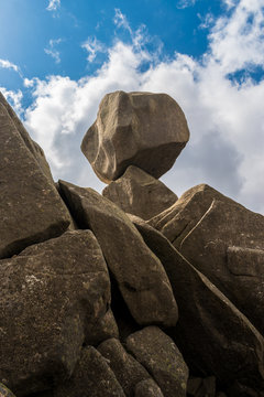Closeup view of Omu di Cagna (Uomo di Cagna) on the island of Corsica. The granite rock is balanced at the top of a peak on the mountain of Cagna, surrounded by clouds and blue sky.