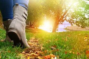 Woman in grey shoes and jeans walking on the autumn forest path with yellow leaves