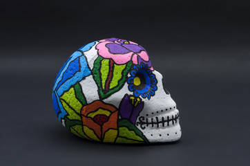 Hand painted styrofoam skull with flowers against black background. Han painted skull for Halloween and mexican Day of the dead decoration