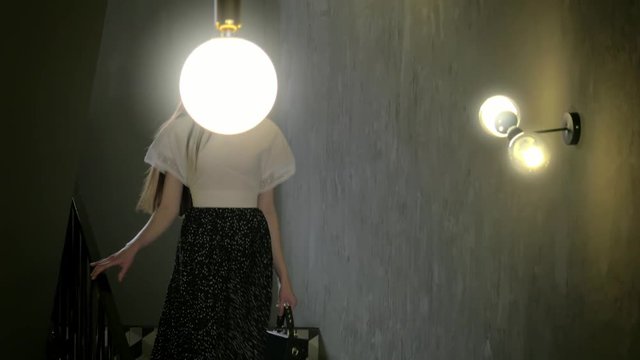 beautiful young Caucasian girl with long dark hair elegantly go down the stairs looking at the camera, lifestyle