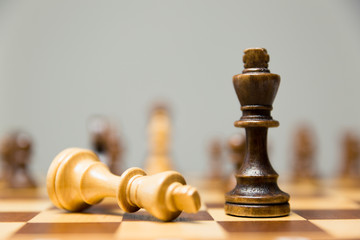 Two King chess pieces on a chessboard with the light king lying on its side at the foot of the victorious dark wood King