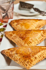 Front, top view, medium distance of three, freshly baked, homemade, cherry  cream turnovers , cooling on a white, rectangular plate, with a silver pie wedge 