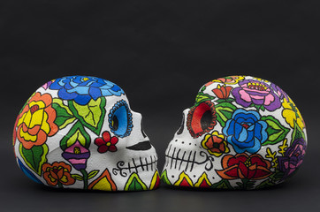 Hand painted styrofoam skulls with flowers against black background. Han painted skulls for Halloween and mexican Day of the dead decoration