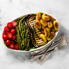 a side dish of vegetables on the holiday table. healthy food for the whole family or dinner at a restaurant on a white marble table. baked potatoes, grilled eggplants, cherry tomato salad 